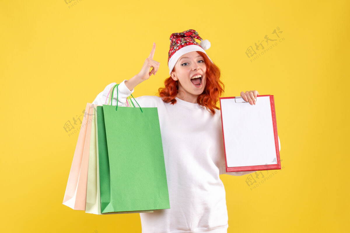 前面黄色墙上拿着购物包的年轻女子的正视图购物微笑圣诞节