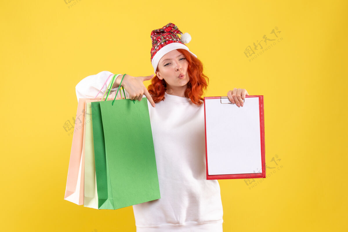 人黄色墙上拿着购物包的年轻女子的正视图包裹微笑抱着
