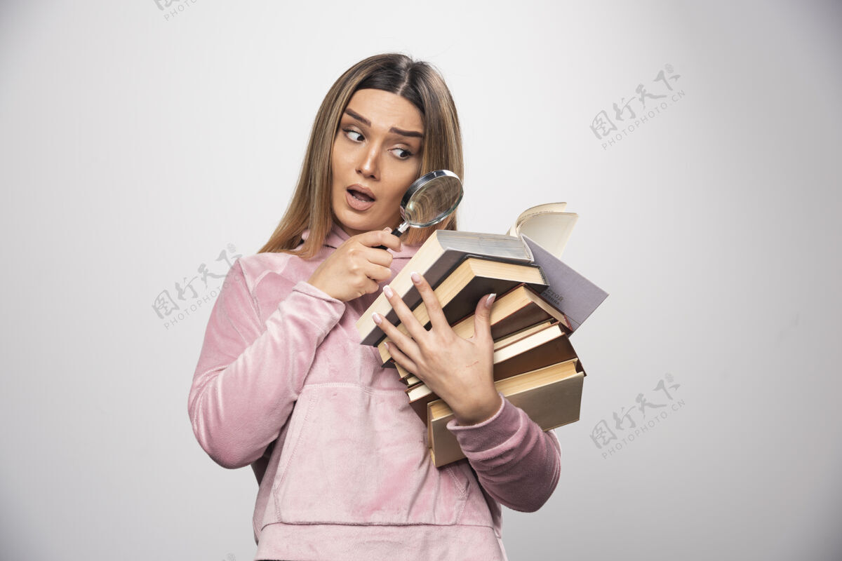 聪明一个穿着粉色衬衫的女孩手里拿着一堆书 正试着用放大镜看上面的书呢金发摆姿势玻璃