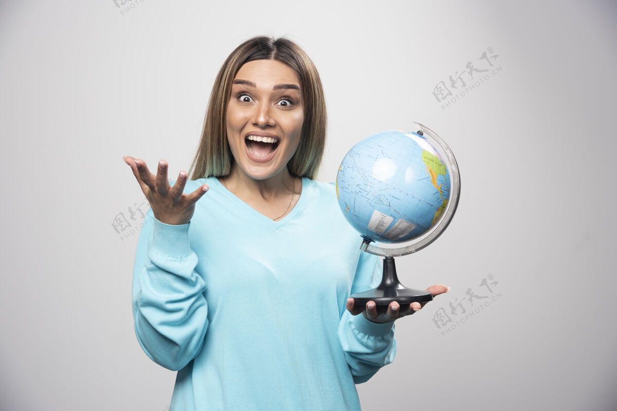 积极穿着蓝色运动衫的金发女孩拿着一个地球仪 猜着地点 玩得很开心世界休闲女人