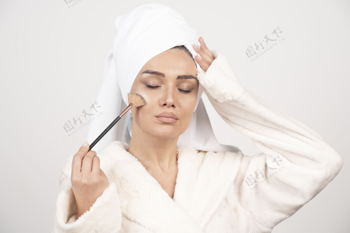 淋浴一个穿着浴衣拿着化妆刷的年轻女人护理女性浴袍