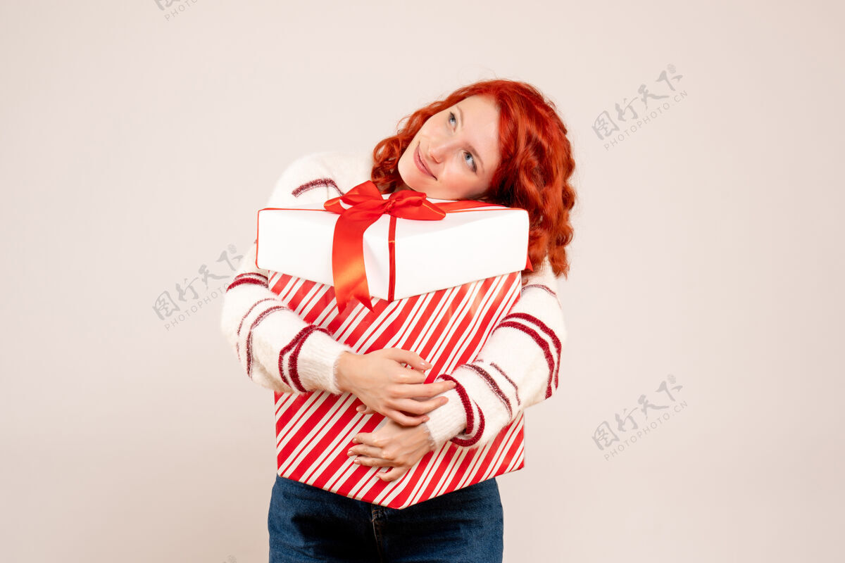 盒子白墙上拿着大礼物的年轻女子的正面图微笑节日前面