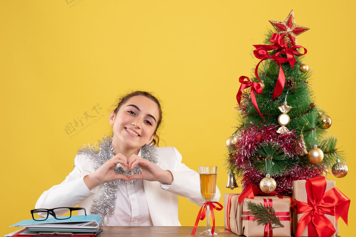 新郎正面图：女医生坐在桌子后面 用圣诞树和礼盒在黄色背景上传递爱坐着人爱情