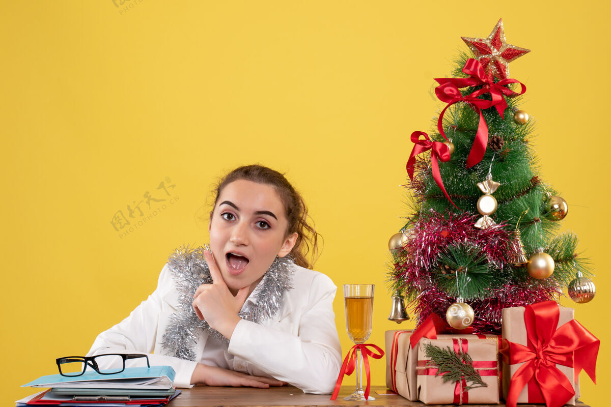 情感正面图：女医生坐在黄色背景的桌子后面 还有圣诞树和礼品盒花前面背景