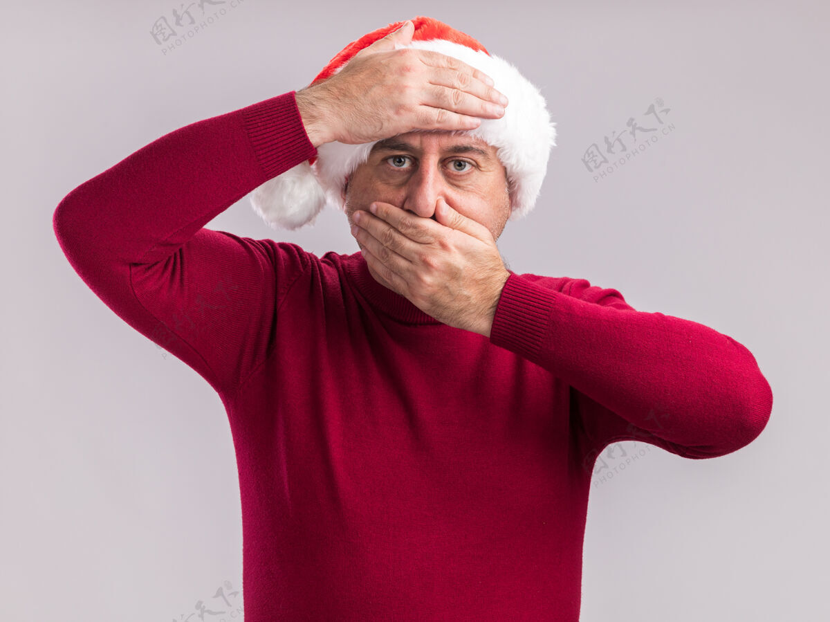 圣诞节中年男子戴着圣诞老人帽 手放在额头上 用手捂住嘴 站在白色背景上看镜头年龄站着中间