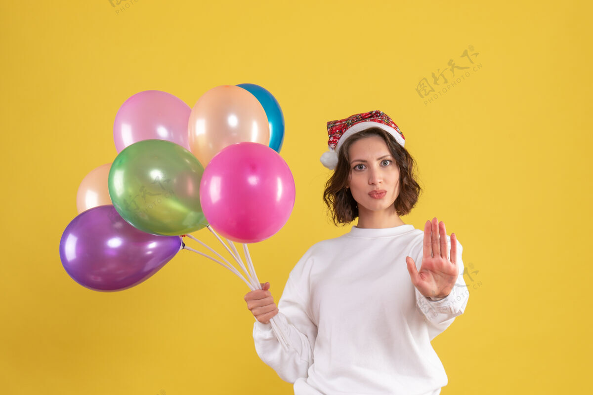 快乐黄色墙壁上手持彩色气球的年轻女子的正视图节日聚会乐趣