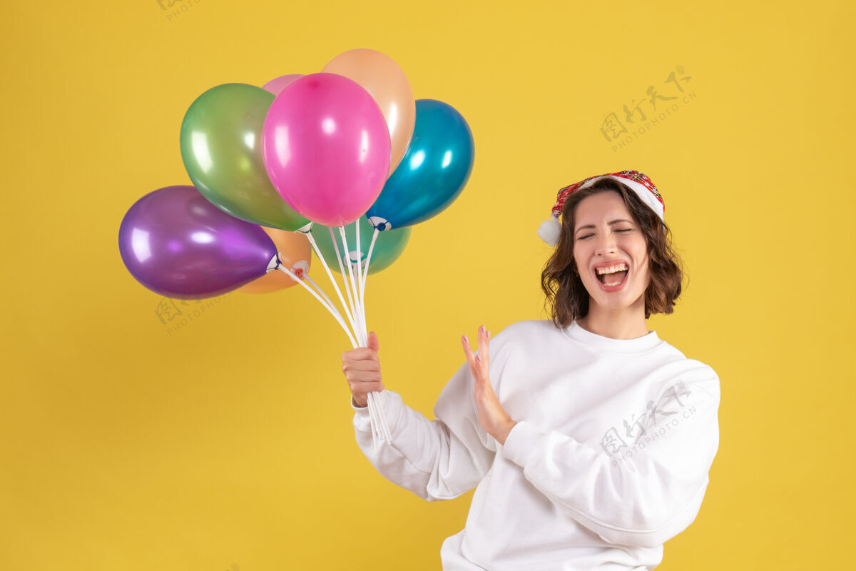 气球黄色墙壁上手持彩色气球的年轻女子的正视图空气多彩节日