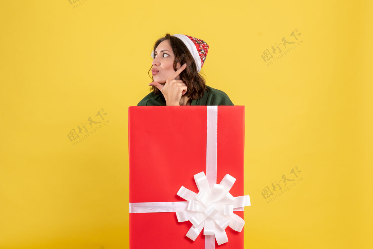 包装站在黄色墙上盒子里的年轻女子的正视图节日里面圣诞节
