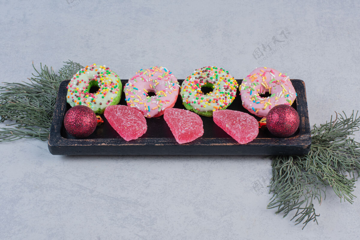 五颜六色美味的甜甜圈 黑色盘子上有洒水器和果酱草莓蛋糕果酱