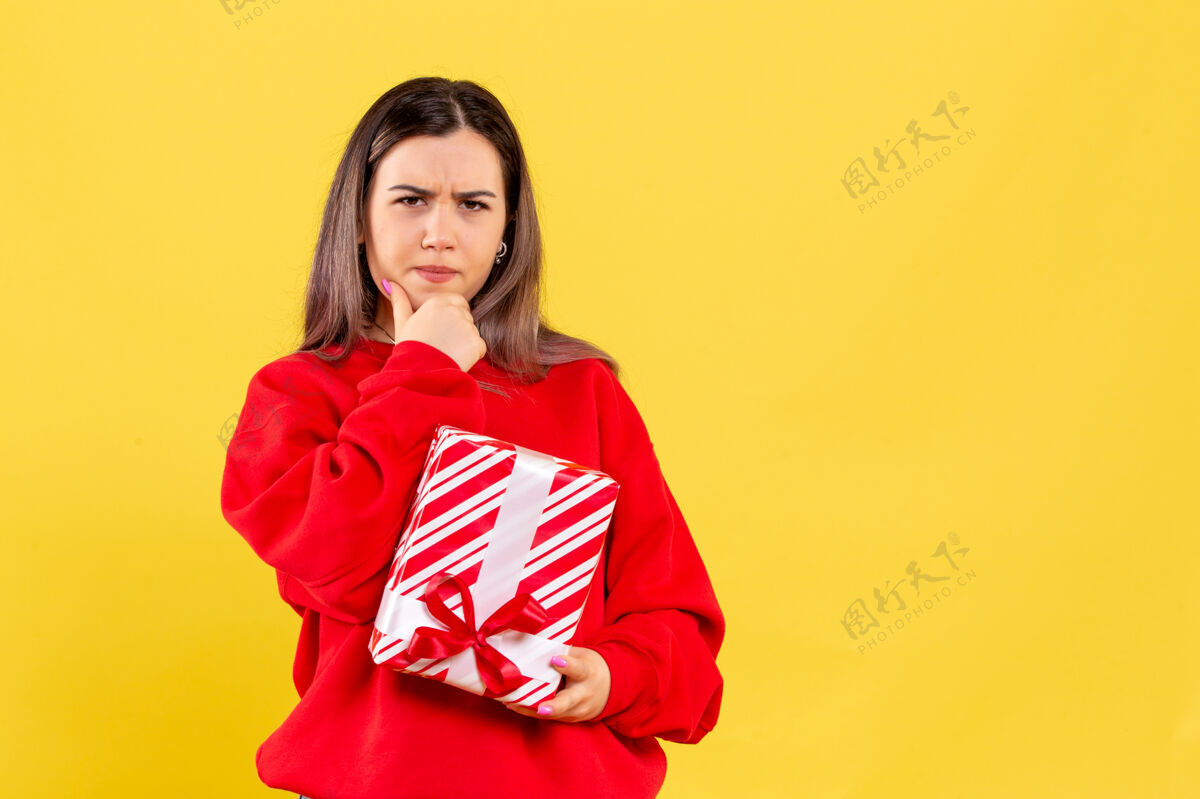 礼物黄色墙上拿着小礼物的年轻女子的正面图庆祝圣诞节漂亮