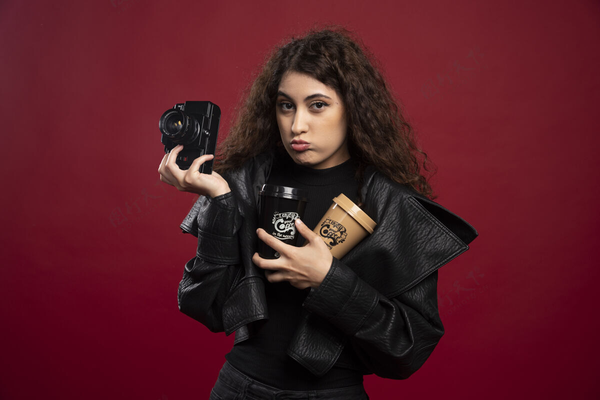 摄影师一个穿着全黑衣服的年轻女人 手里拿着杯子和相机外卖黑色年轻