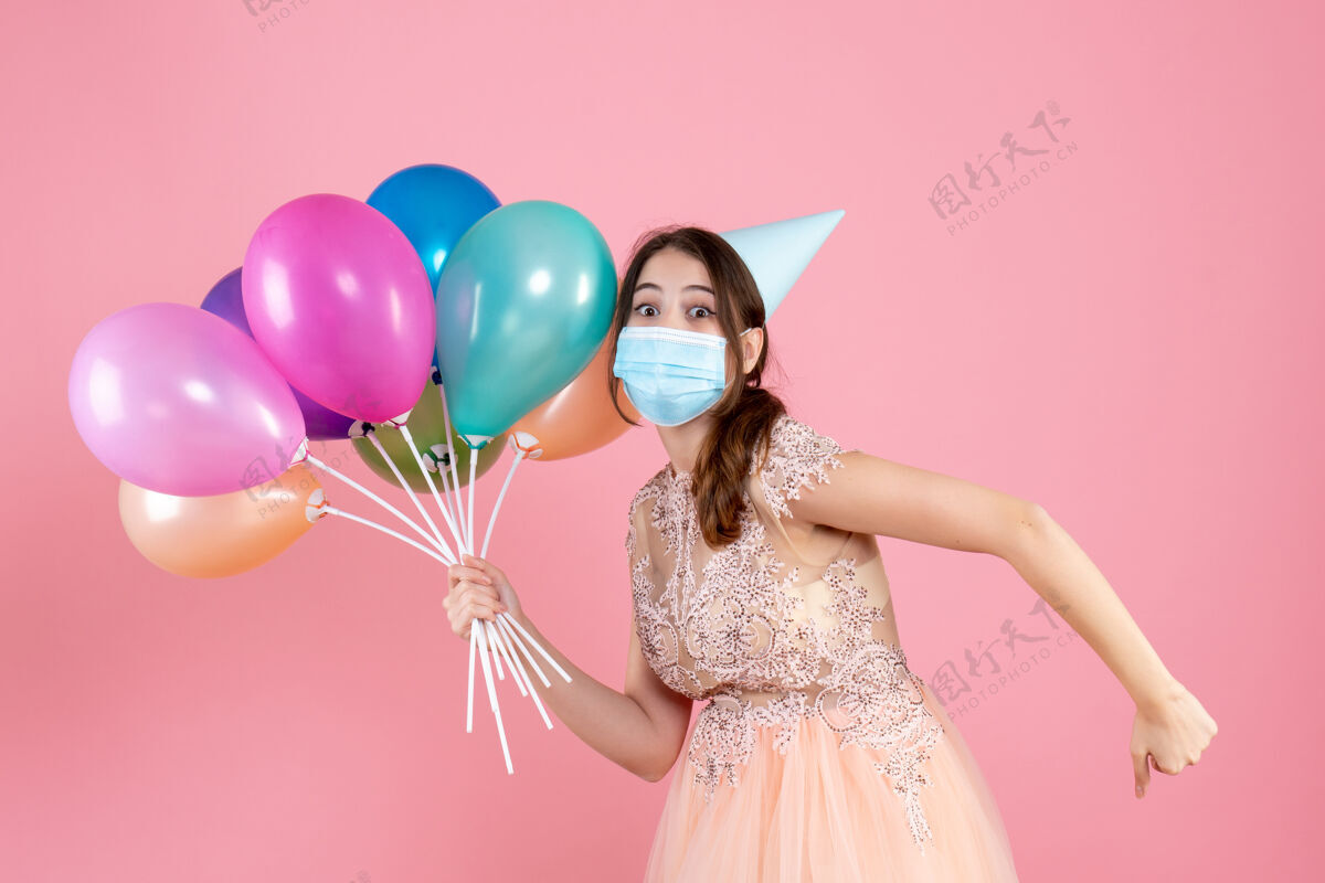 庆祝戴着派对帽的大眼睛女孩一边跑一边拿着粉色的彩色气球气球聚会生日