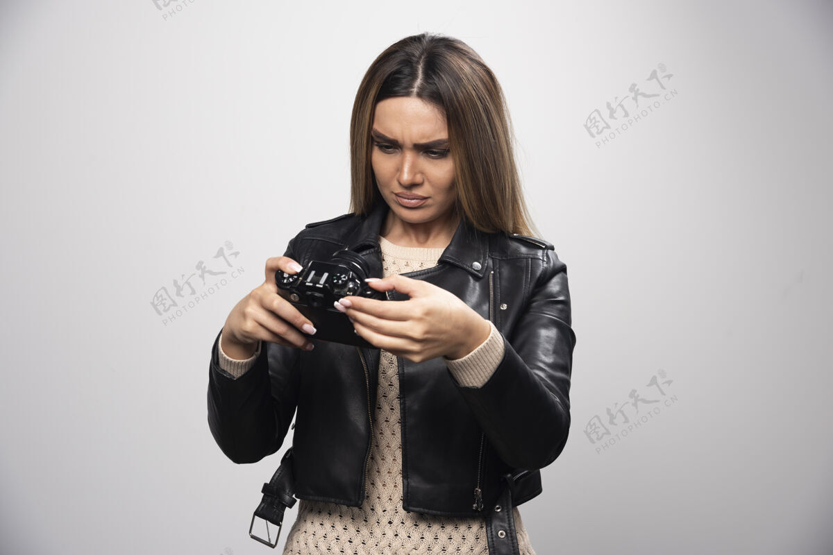相机一个穿着黑色皮夹克的金发女孩在看她的单反照片 看起来很不满意随意思考女人