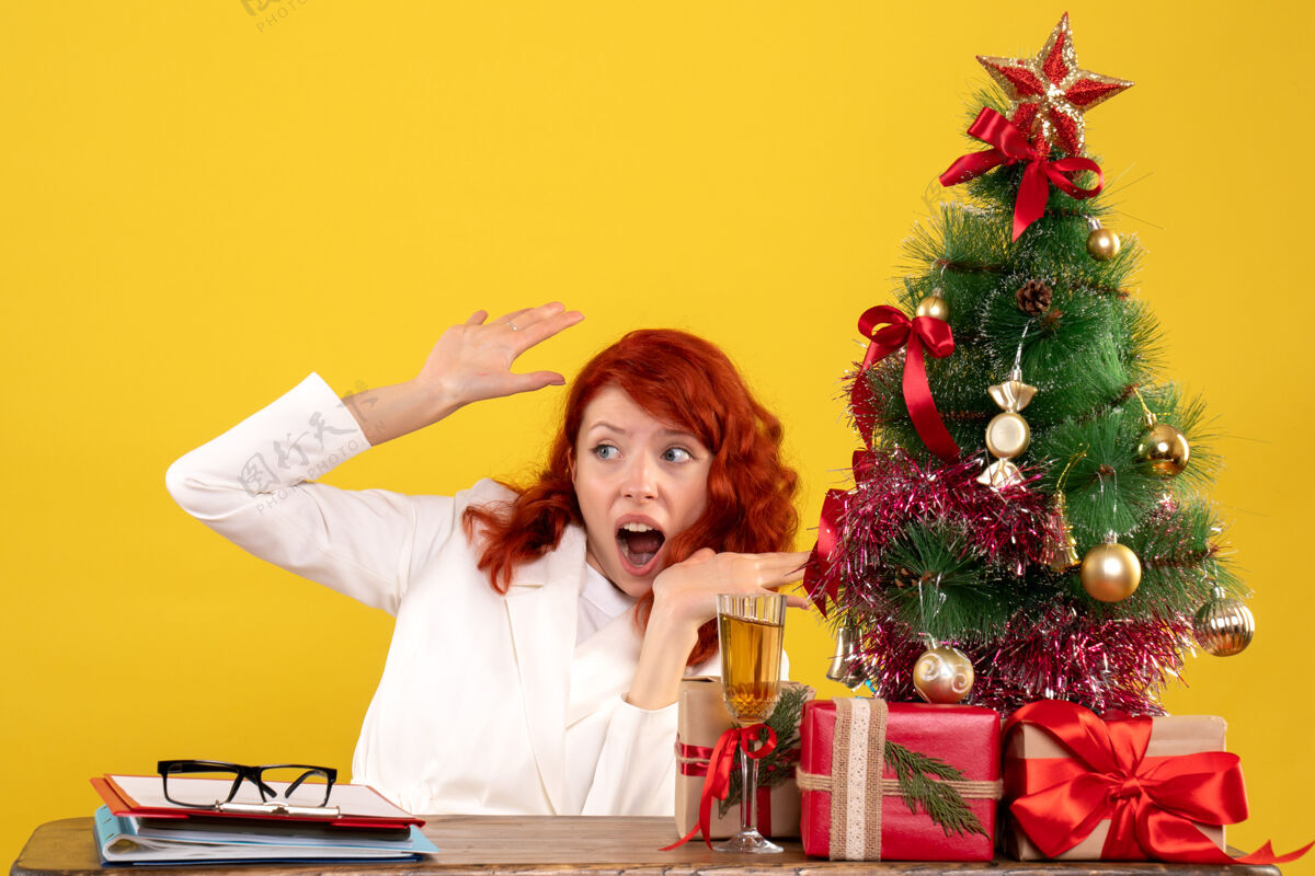 女女工人坐在桌子后面 手里拿着圣诞礼物和黄色的圣诞树圣诞节办公室桌子