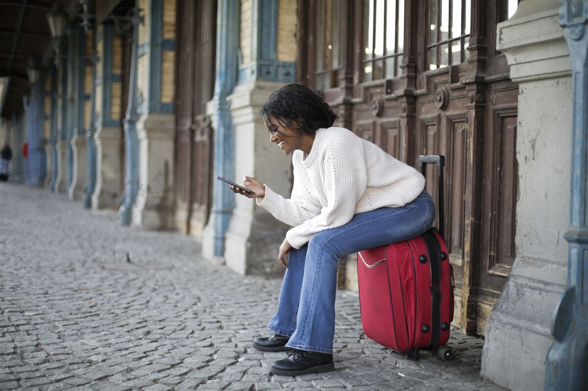 手机美丽的镜头 一个女人穿着白色长袖坐在红色的行李上技术手机年轻人
