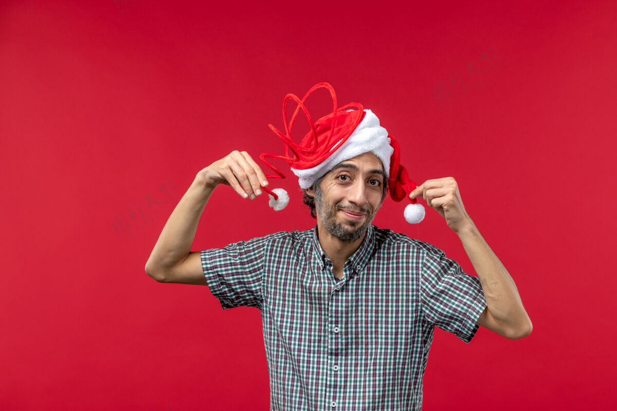 节日红墙上戴着滑稽玩具帽的年轻人的正面图圣诞节男性搞笑