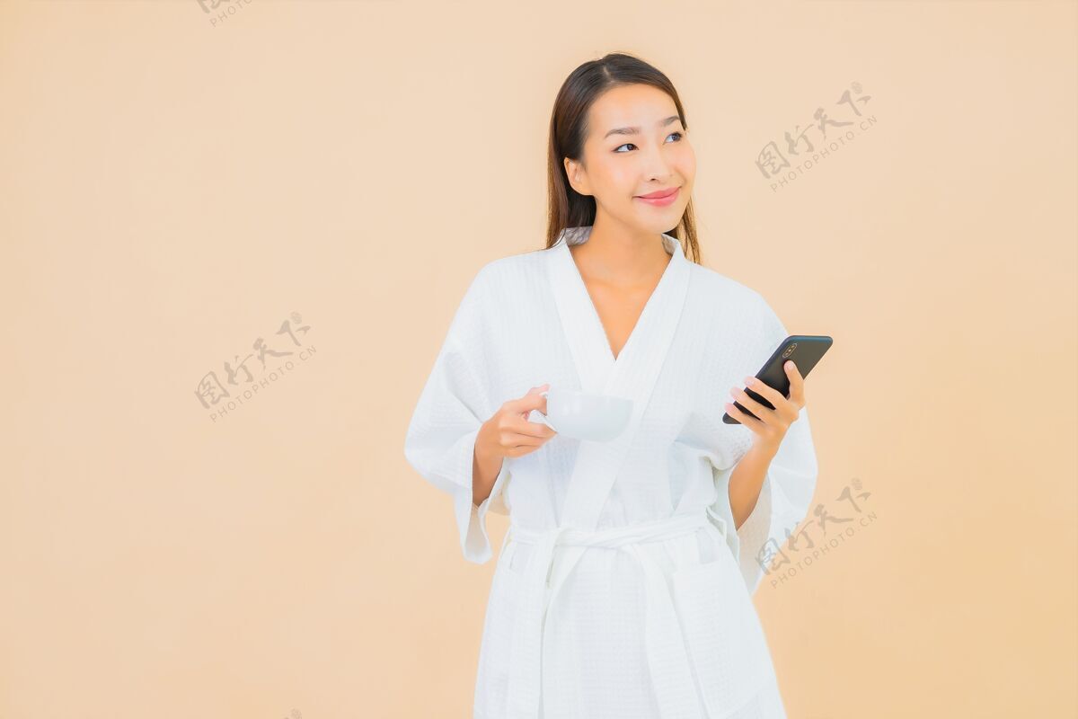 坐着用米黄色智能手机描绘美丽的亚洲年轻女子手机早晨电话