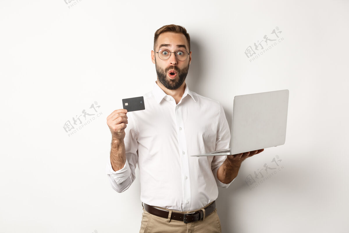 成人网上购物惊讶的男人拿着笔记本电脑和信用卡 在网店购物 站着笔记本电脑买家使用