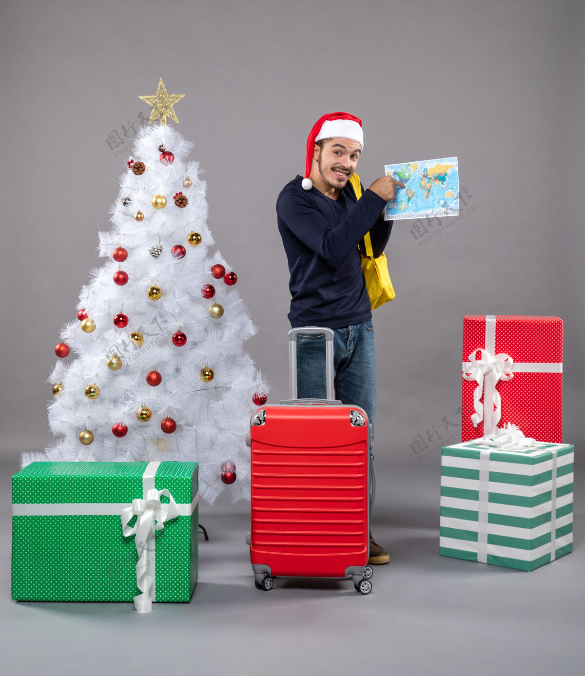 检查兴奋的圣诞老人背着黄色的背包在灰色的圣诞树旁查看地图礼物男人近