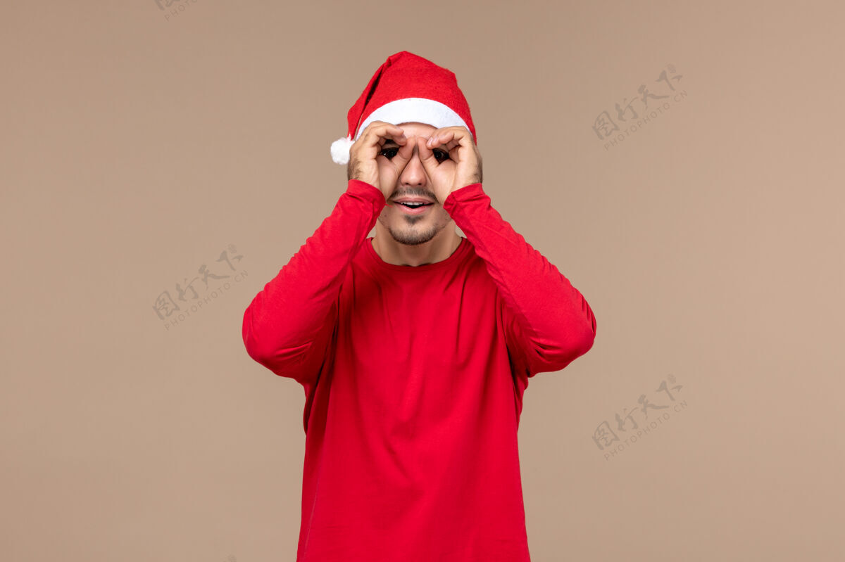 人正面图年轻男性透过手指看棕色背景圣诞假期感慨脸男性手指