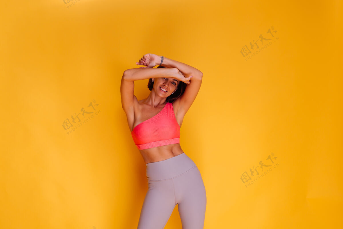 动机年轻健壮的女人穿着运动服 时髦的上衣和紧身裤 对着黄色的墙壁摆姿势有力强壮锻炼