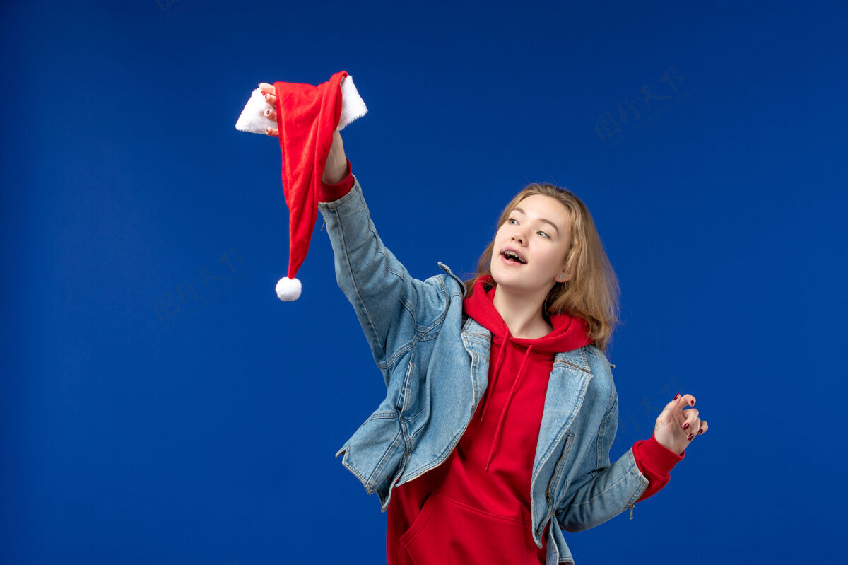 快乐正面图蓝色背景上戴着红色帽子的年轻女性圣诞色新年年轻的女性人吹