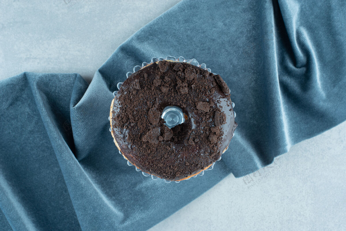美味把一个甜甜圈放在一个小玻璃盘上 放在大理石上起皱的桌布上上釉甜味美味