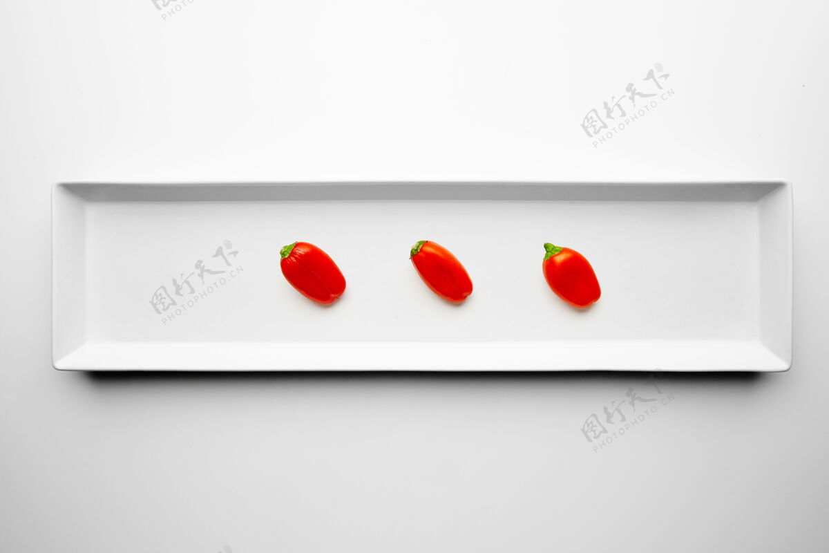 美味三个红辣椒隔离在白色背景上的矩形陶瓷板的中心切块成分食物