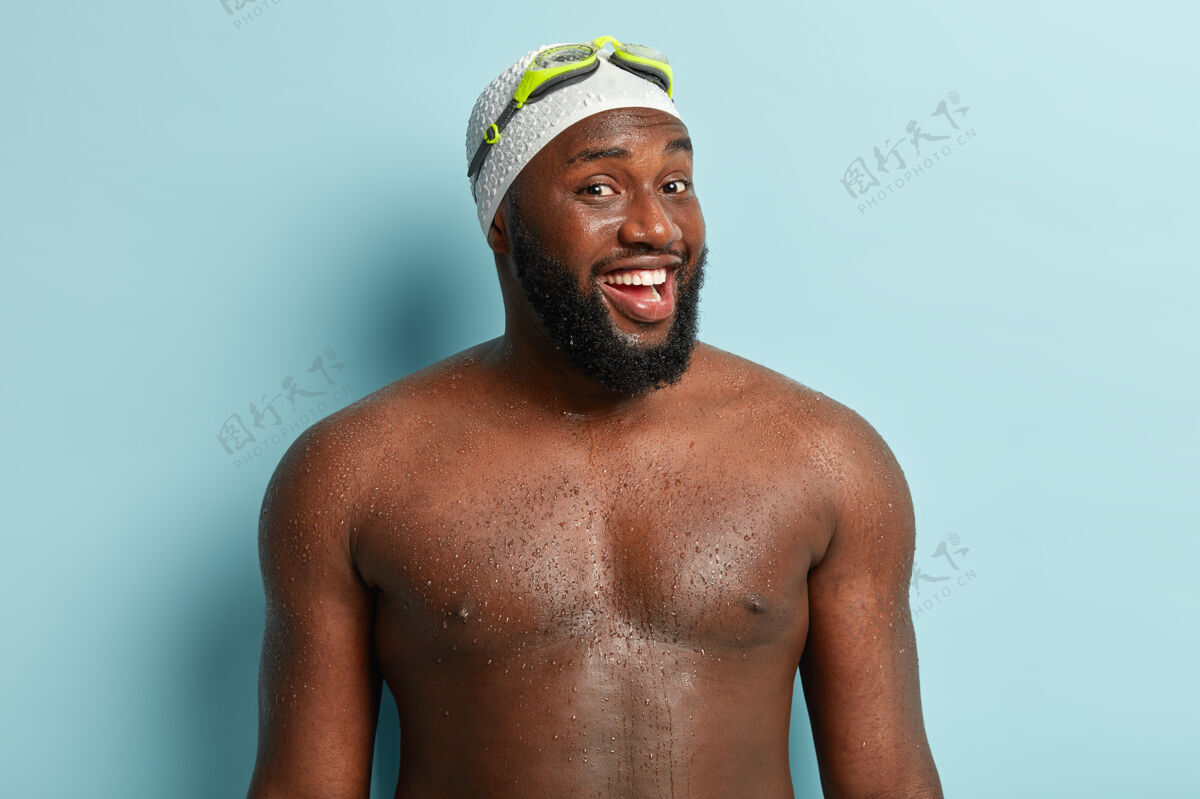 大笑健康的黑人 体形健壮 是一名专业的游泳运动员 从水里出来 感觉放松 充满活力 戴着泳帽 护目镜 隔离在蓝色的墙上身体运动员胡须