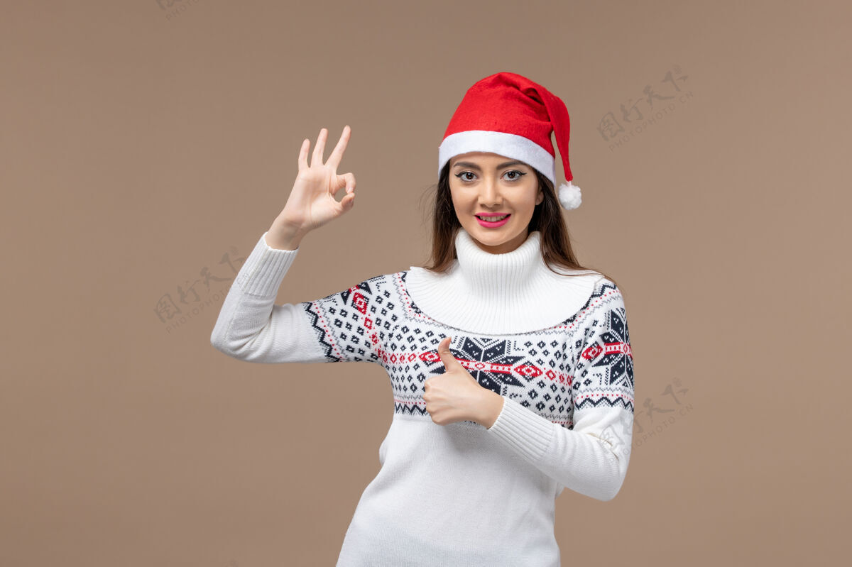 棕色正面图棕色背景上戴着红帽子微笑的年轻女性感慨圣诞新年人物微笑人物