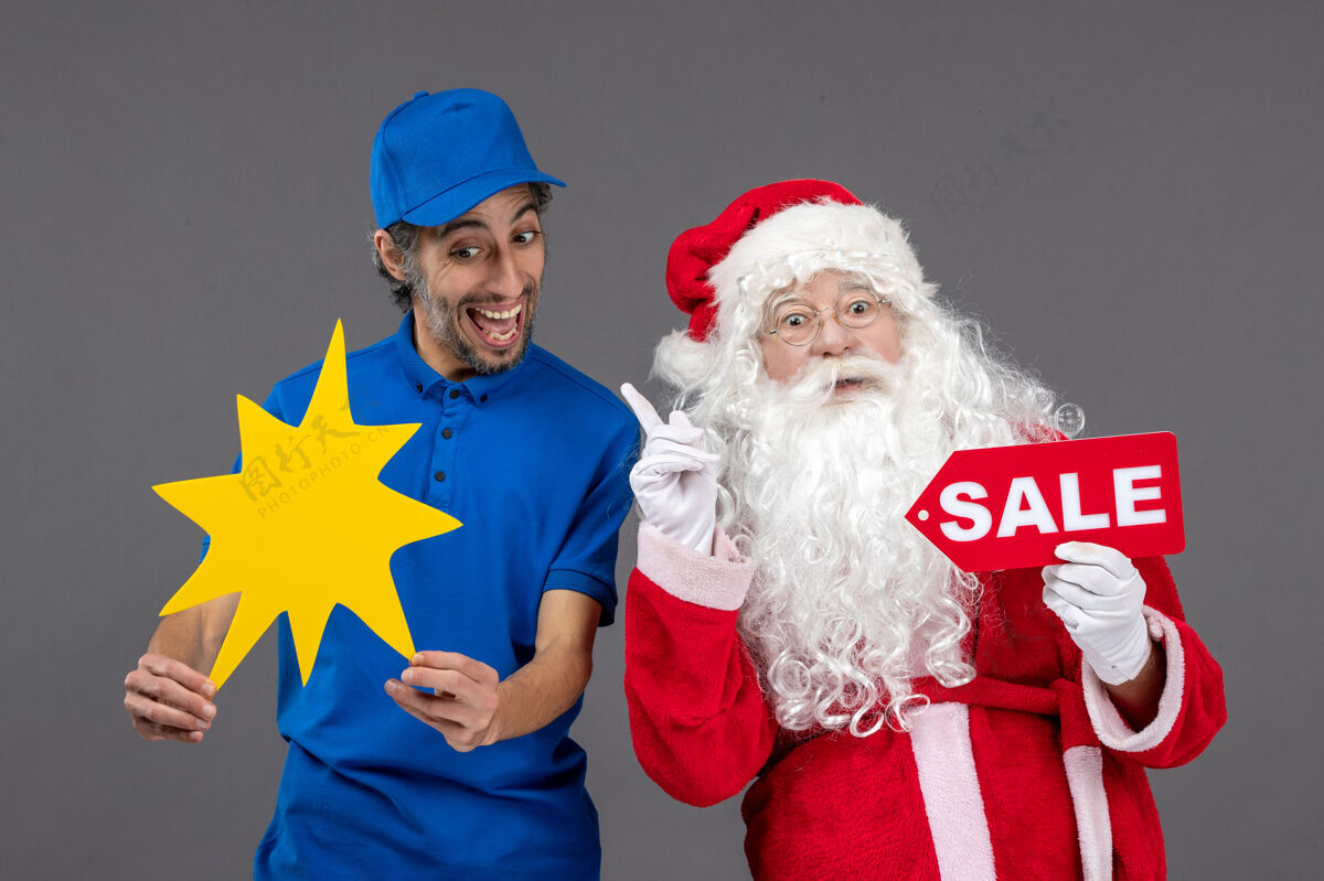 圣诞圣诞老人的正面图 男性信使手持销售横幅 灰色墙上有黄色标志男人圣诞老人人