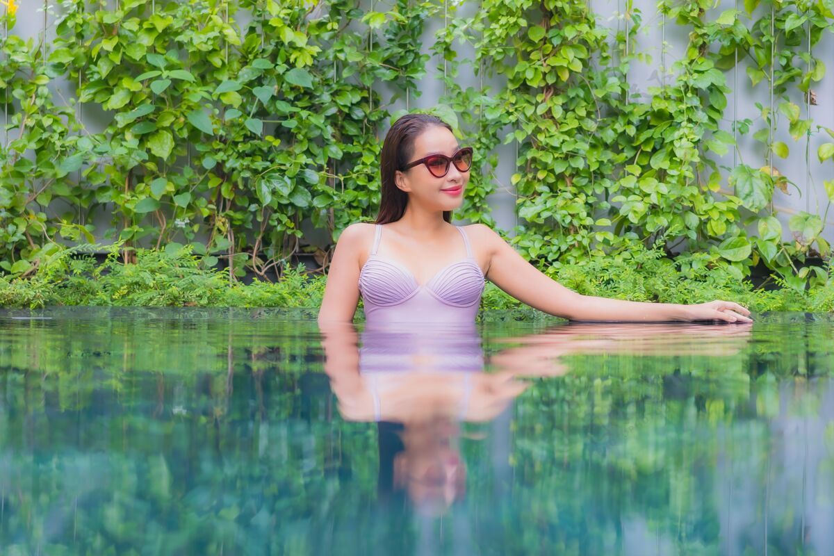 棕褐色肖像美丽的亚洲年轻女子放松微笑休闲在酒店度假村的室外游泳池周围海滩泳池边身体