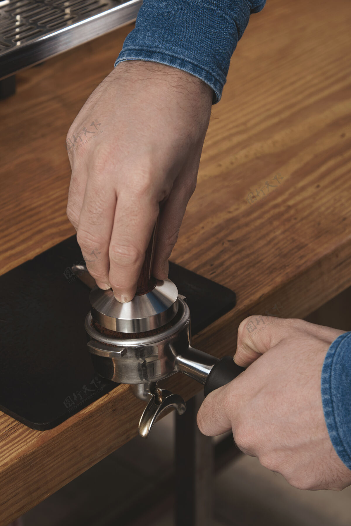 热的咖啡师用捣固机把磨碎的咖啡压进咖啡馆的一个便携式过滤器 放在厚厚的木桌上专业咖啡酿造卡布奇诺分配器饮料