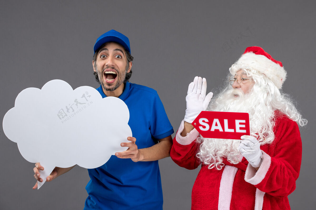 人圣诞老人的正面图 男信使手持白云招牌 在灰色墙上出售快乐销售庆祝
