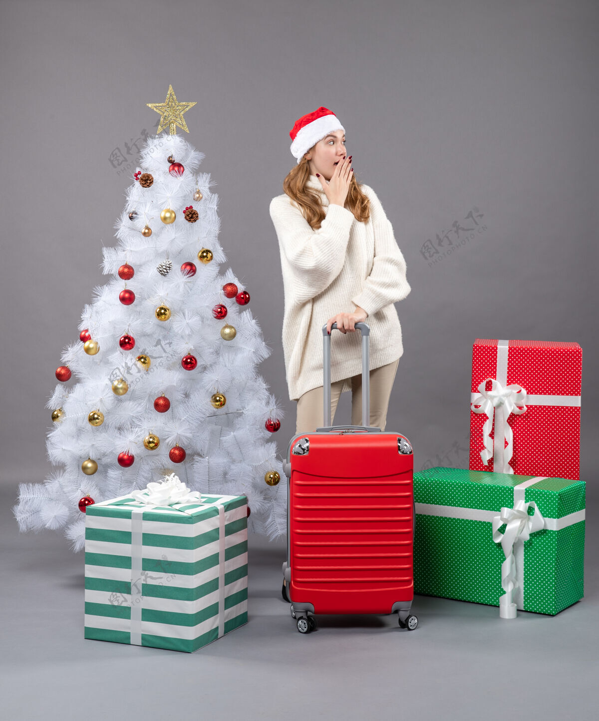 圣诞老人前视图惊讶的女孩与圣诞帽把手放在她的鼠标站在圣诞树和礼物附近站着女孩圣诞