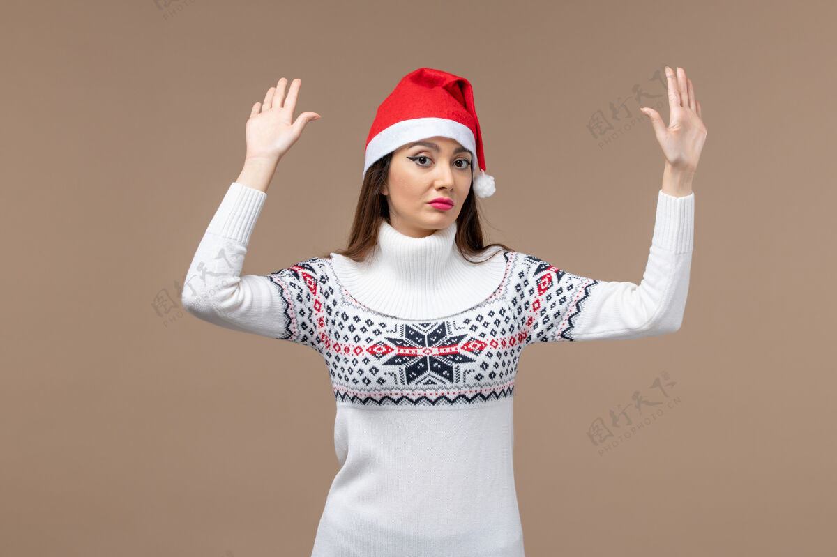 肖像正面图棕色背景上戴着红色圣诞帽的年轻女性圣诞假期感慨开朗年轻情感