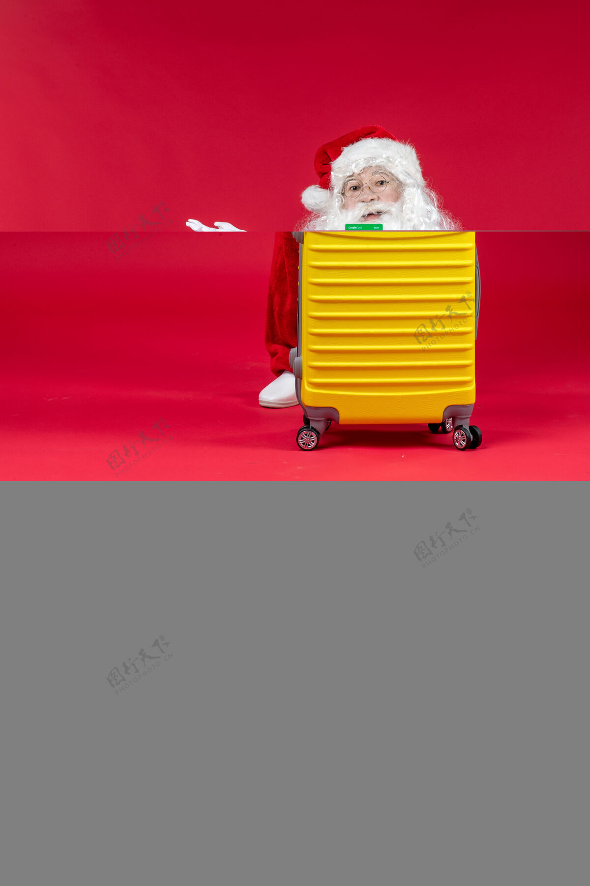 圣诞老人红墙上挂着黄色袋子 手里拿着绿色银行卡的圣诞老人的正视图圣诞圣诞老人节日