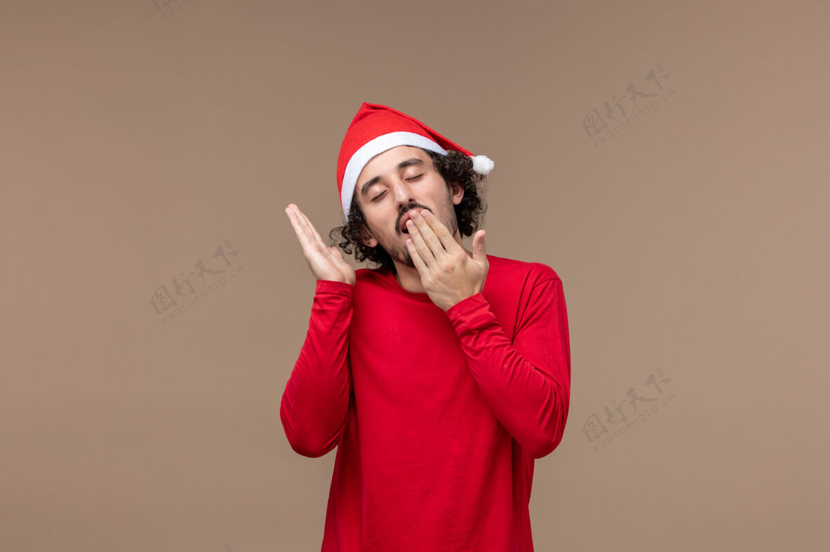 尝试正面图年轻男子打哈欠 试图在棕色背景上睡觉圣诞节情绪圣诞节睡眠歌手