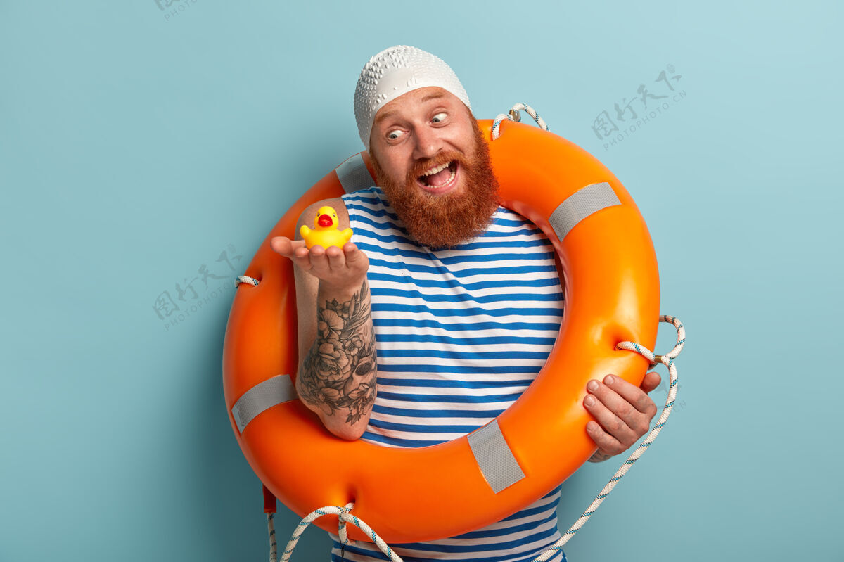 救生员顽皮快乐的男人 红浓密的胡子 抱着小玩具鸭 在岸上玩休息娱乐冒险