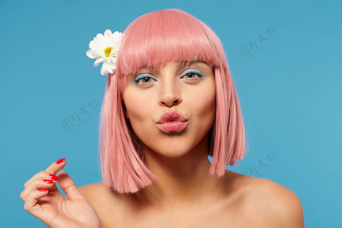 淑女年轻漂亮的粉红色头发女性的肖像 鲍勃的发型 在空中亲吻她的嘴唇 同时积极地看着相机 在蓝色背景上摆姿势举起手修剪肖像肩部