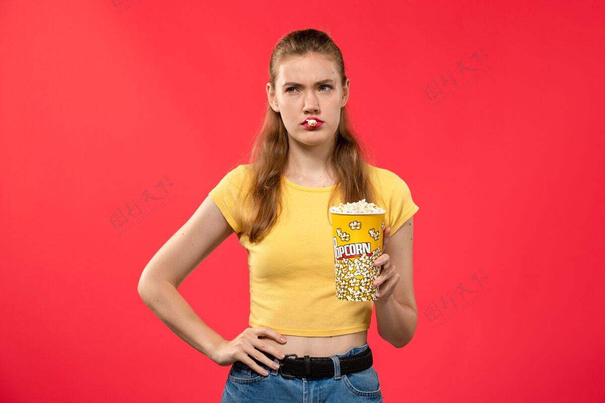 爆米花前视图年轻女性在电影院拿着爆米花包 在红墙电影院摆姿势女性趣味电影观点年轻女性电影