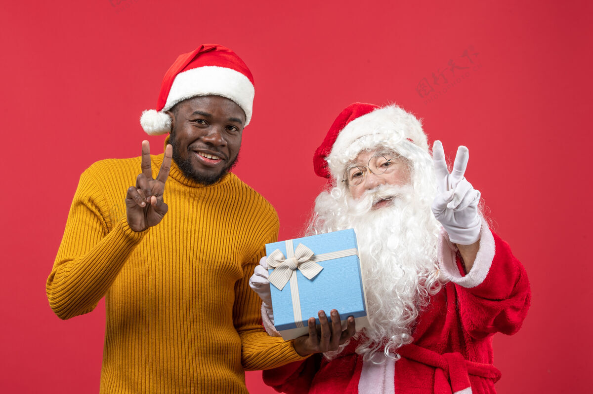 礼物红墙上的圣诞老人和拿着礼物的年轻人的正视图前面圣诞老人年轻