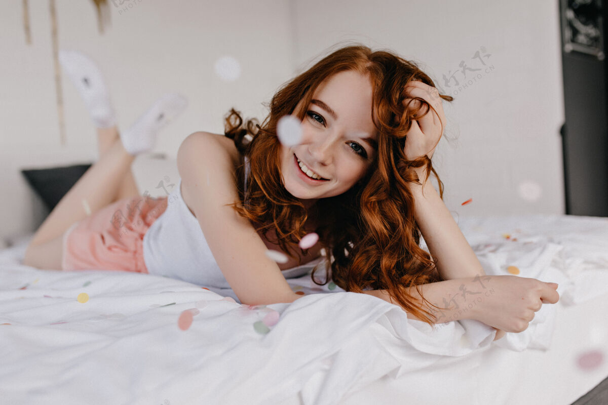 美丽令人惊艳的欧洲年轻女士躺在床上看着愉快的红发女孩享受周末早晨的室内摄影醒快乐积极