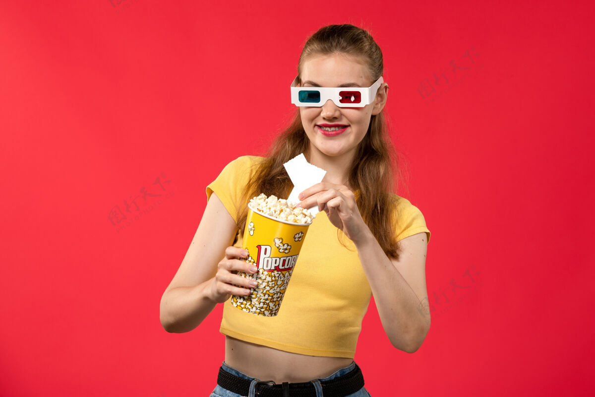 电影院前视图年轻女性在电影院拿着爆米花包在红墙电影院的d太阳镜年轻女性女电影