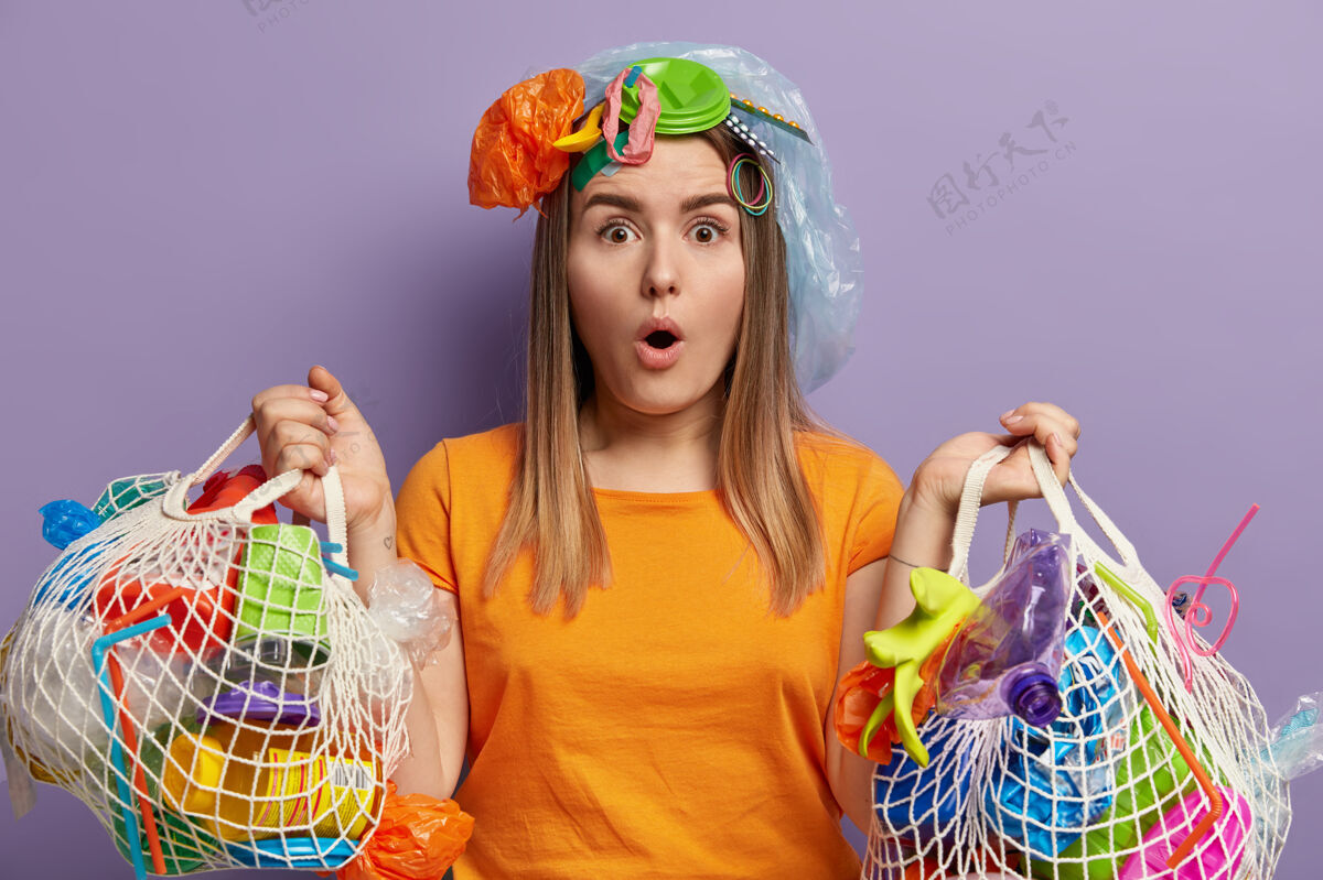 负责一脸惊讶的女志愿者 捡垃圾 拿着两个网袋 穿着橙色t恤 不敢相信她打扫了整个地盘 靠着紫色的墙 回收垃圾志愿者保存白种人