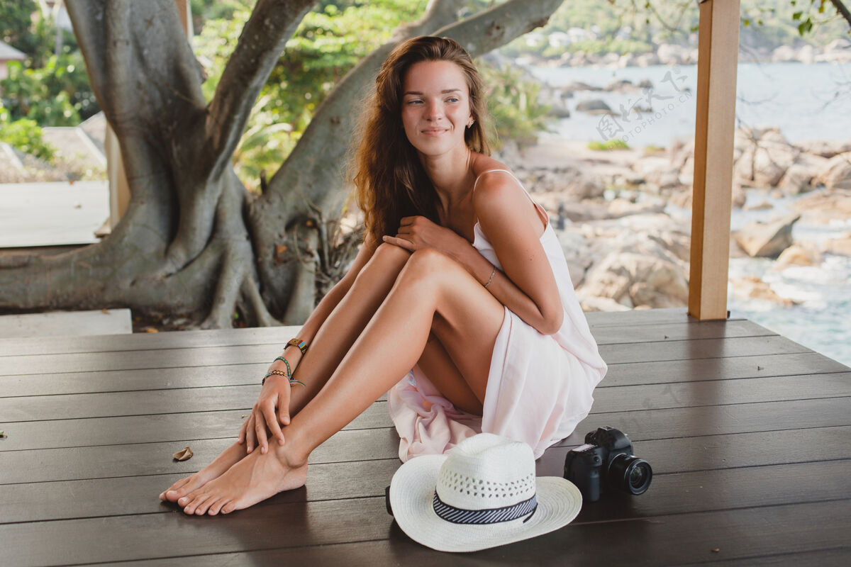 摄影师年轻女子光着脚坐在地板上 穿着苍白的连衣裙 微笑着 自然美丽 草帽 数码相机 微笑放荡不羁休闲