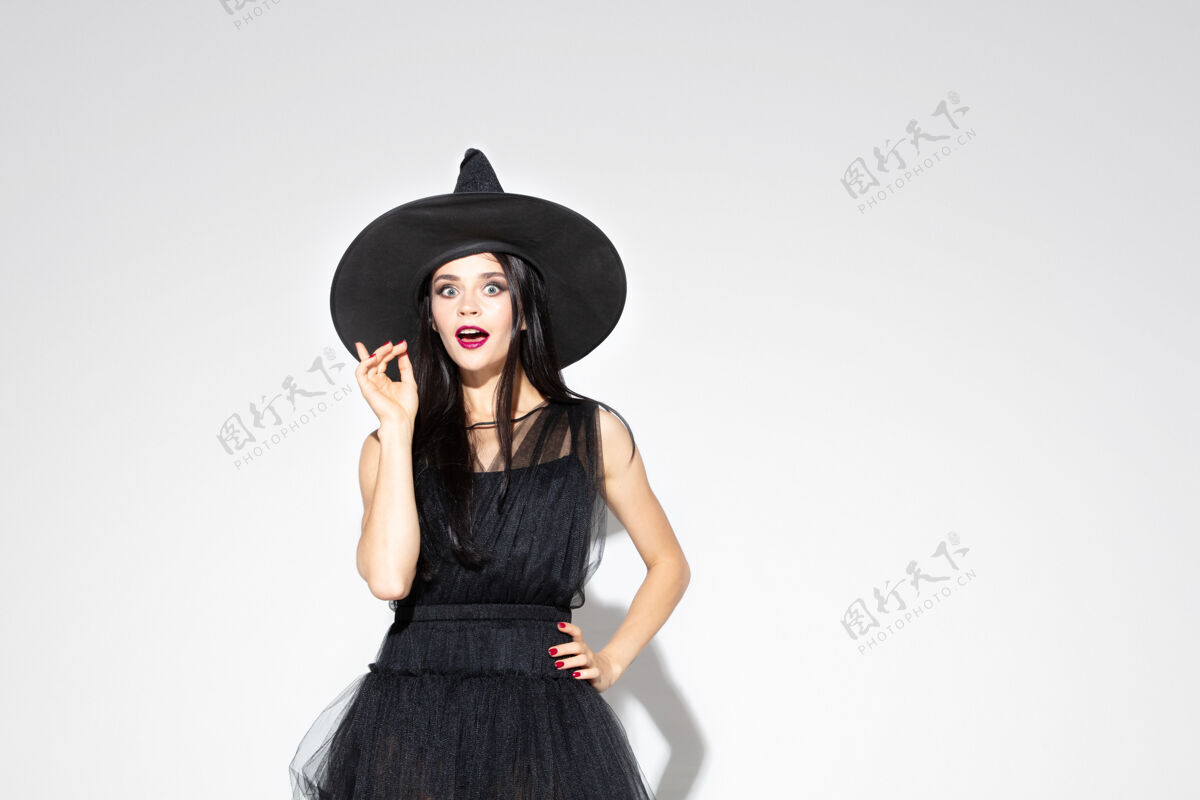 魔术年轻的黑发女子 戴着黑帽子 穿着白色背景的服装迷人的白人女模特万圣节 黑色星期五 网络星期一 销售 秋季概念复制空间指向上性感女孩秋天