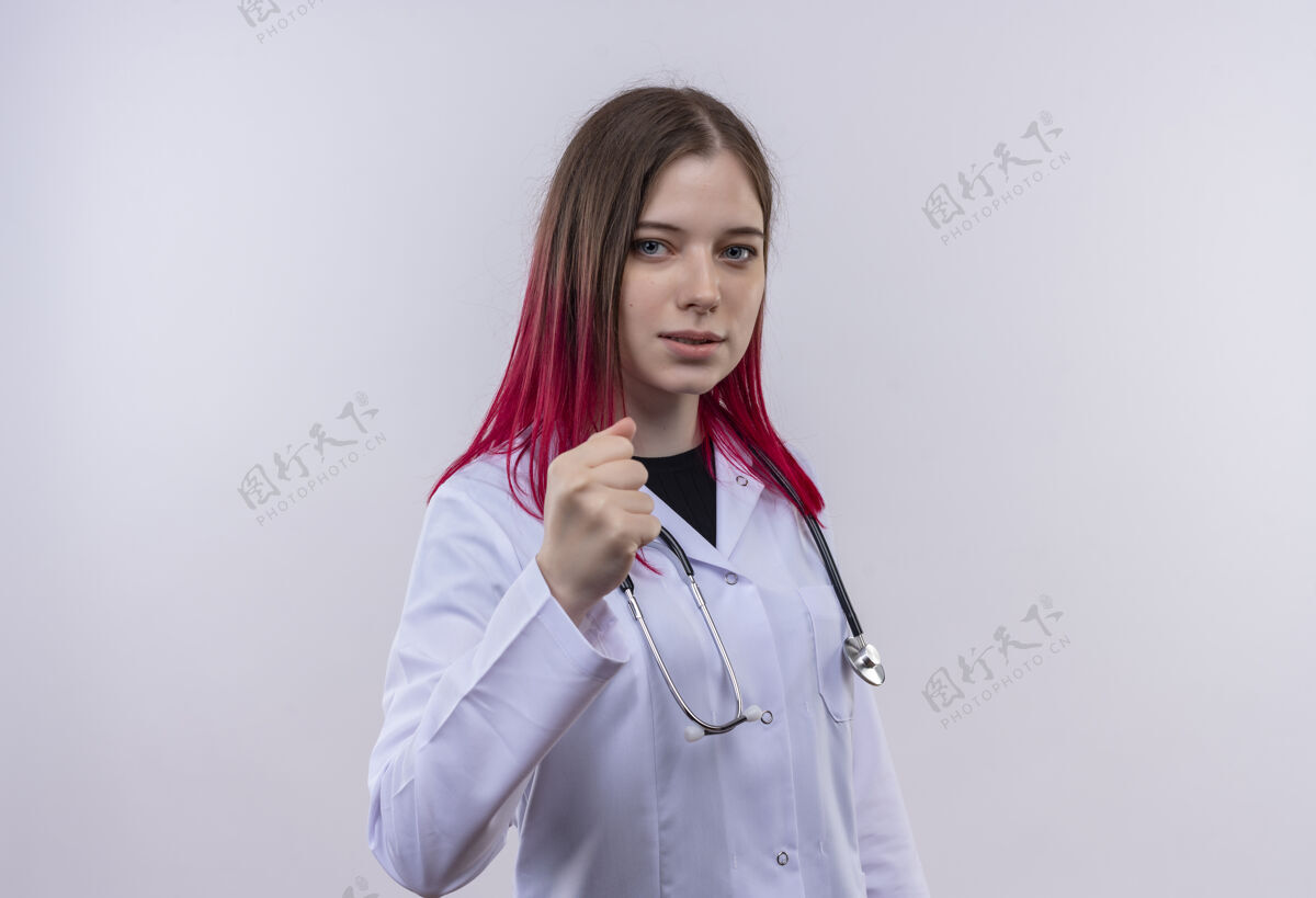 听诊器穿着听诊器医用长袍的严格的年轻医生女孩在孤立的白色背景下向镜头伸出拳头拳头医疗白