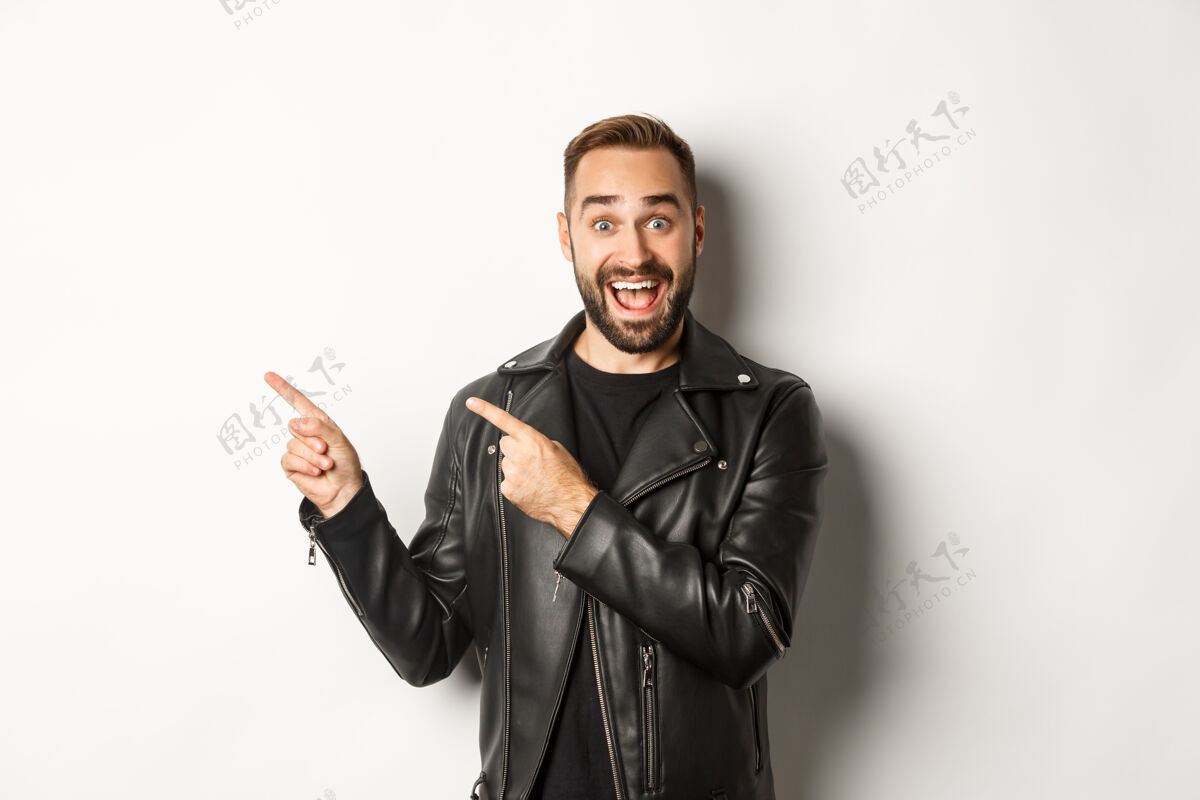 摩托车手一个穿着黑色皮夹克的自信男人 指着促销活动的左指指着左边时尚胡须