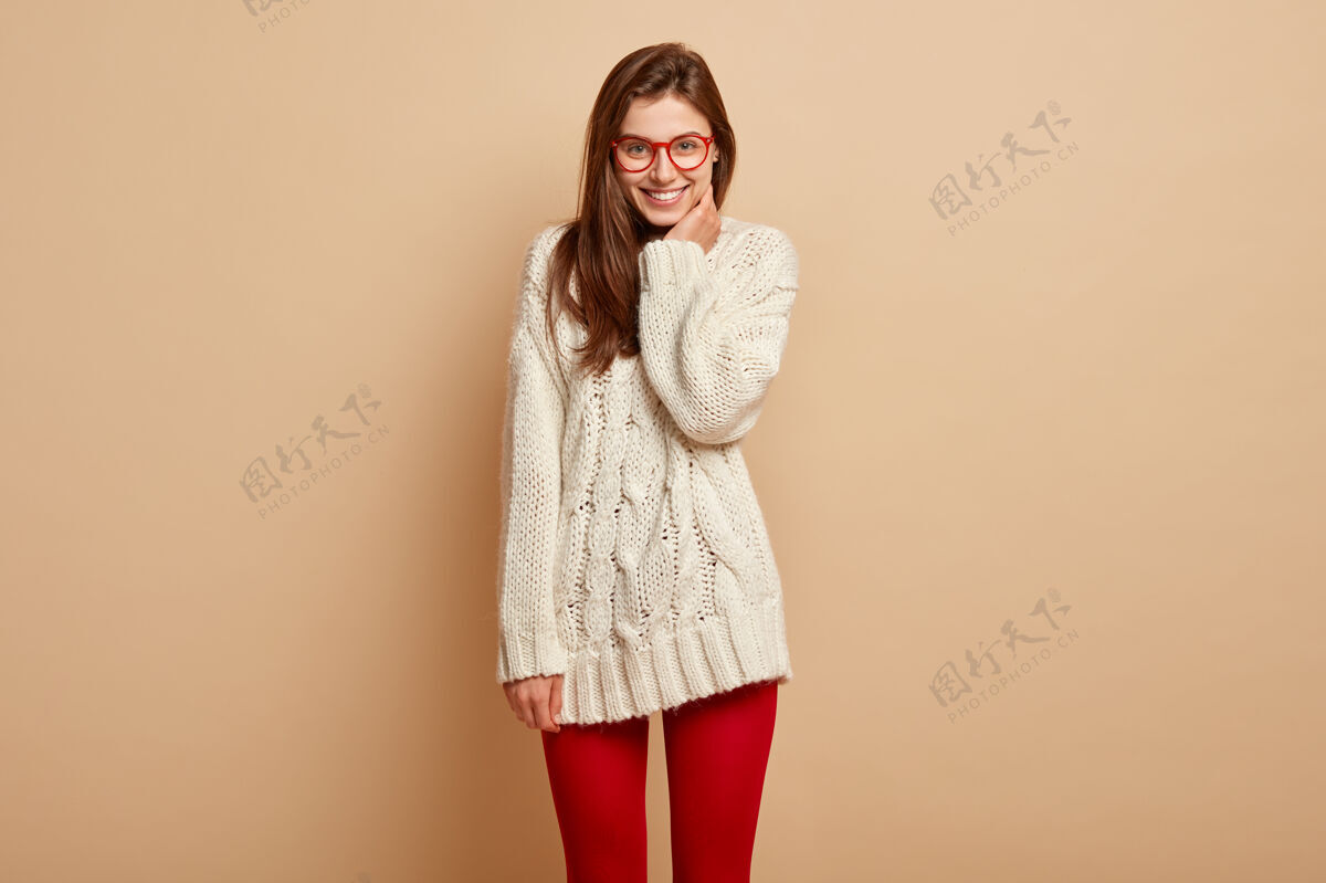 牙齿漂亮的年轻女子微笑着在室内摆姿势 有幸福感 听到好消息 穿着白色套头衫和红色紧身衣 露出完美的牙齿 享受美好的一天欢笑表情连裤袜